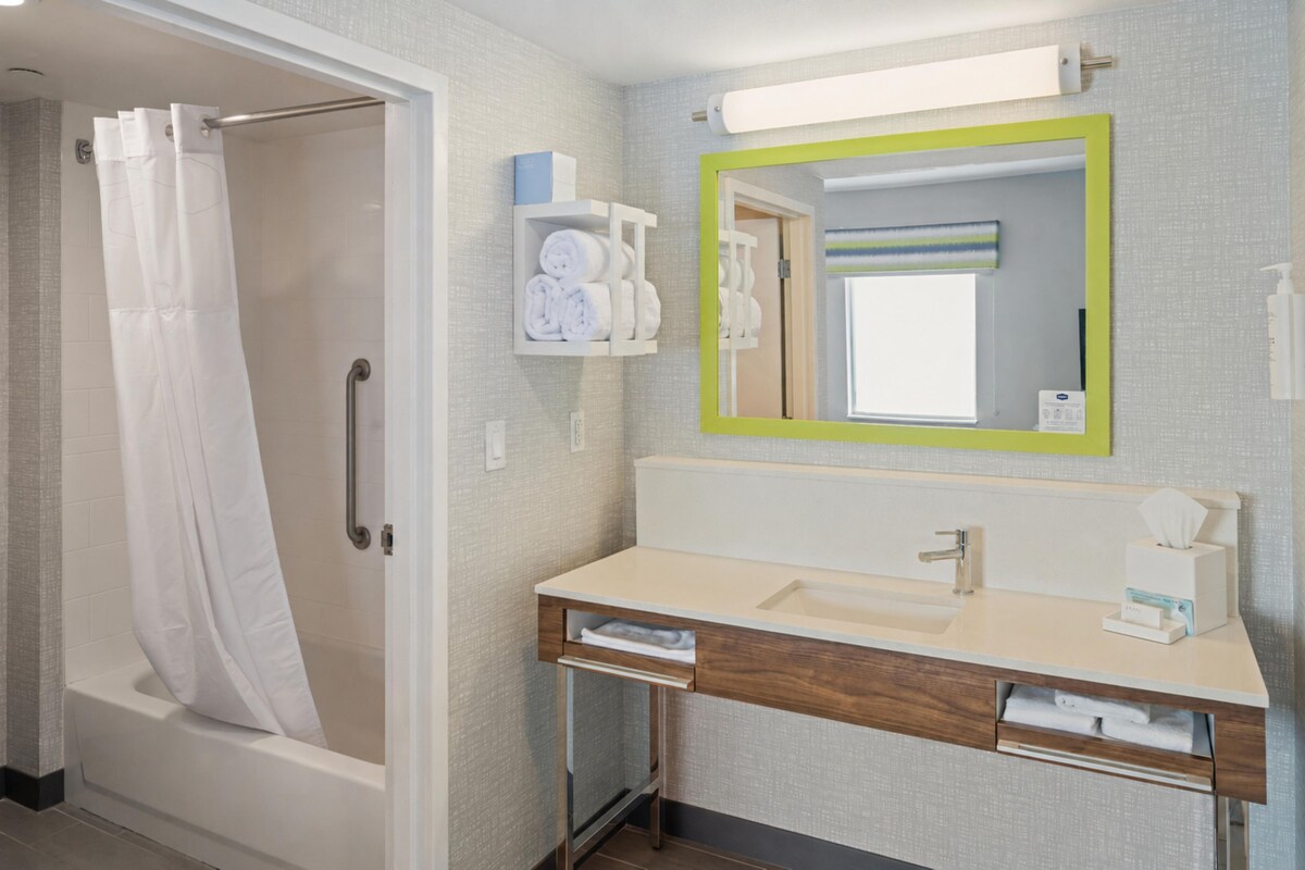 A bathroom with a shower, a sink, a mirror, and a towel rack.