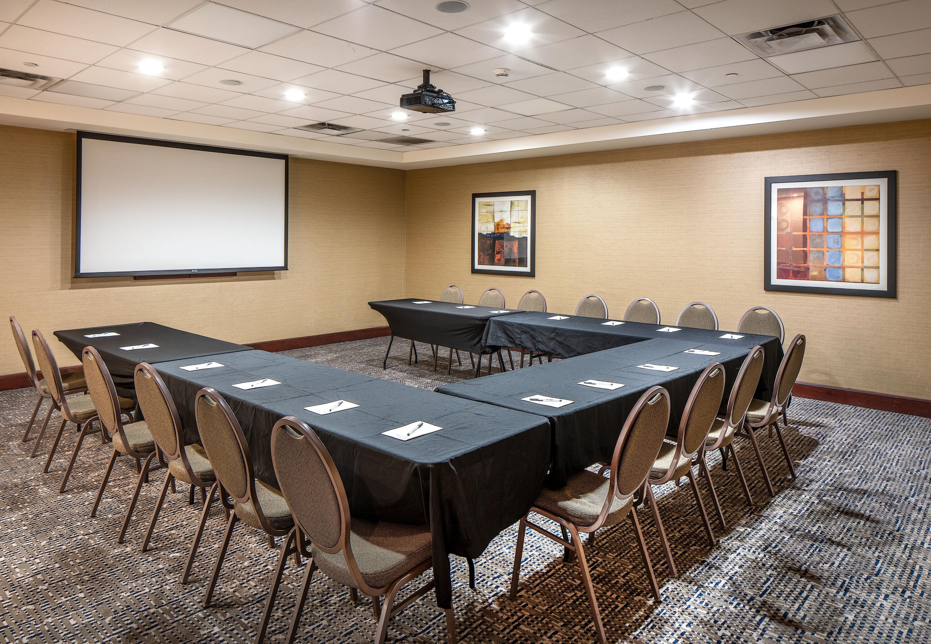 A conference room with a long table, chairs, a projector screen, and a carpeted floor.