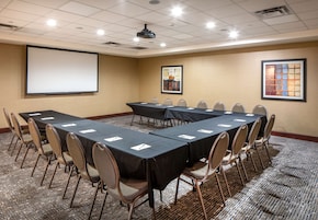 Una sala de conferencias con una pantalla grande, varias mesas y sillas.