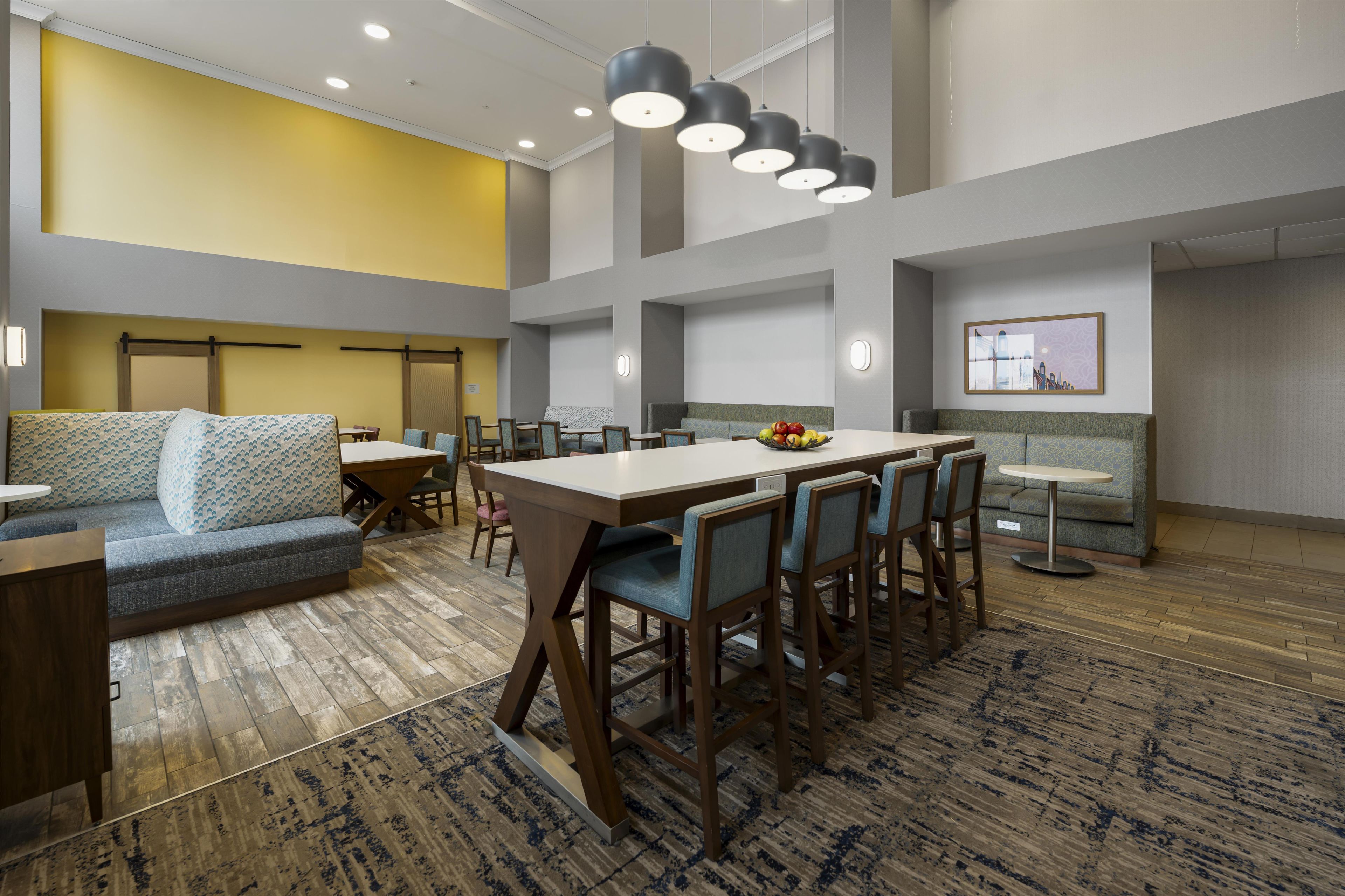 A hotel lobby with a seating area, a long table with chairs, a sofa, and a small round table with a fruit bowl.