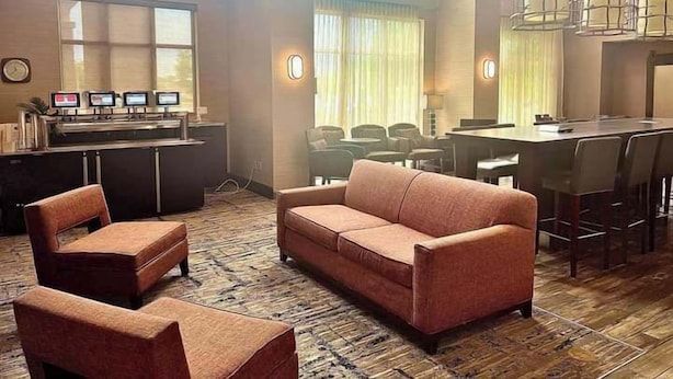 Un hall d’hôtel comprenant un canapé, des fauteuils, un comptoir d’accueil et un espace repas.