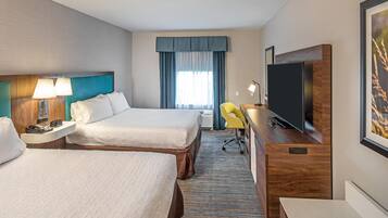 A hotel room with two beds, a desk, a television, and a chair.