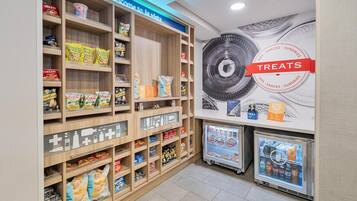 Una sección de aperitivos con estantes llenos de diferentes productos envaselados y un refrigerador exhibidor.