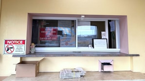 A window with a 'NOTICE' sign prohibiting firearms, a 'NIGHTLY CHECKING DESK' sign, and a 'CHECKING OUT?' sign with a key drop area. - Red Carpet Inn & Suites Lima (Lima)