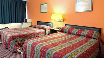 Une chambre d’hôtel avec deux lits, chacun recouvert d’une couvre-lit aux motifs rouges et dorés, une table de chevet avec une lampe et une fenêtre avec des rideaux foncés.