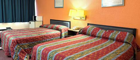 Habitación de hotel con dos camas, cada una con una colcha de diseño rojo y dorado, una mesita de noche con una lámpara y una ventana con cortinas oscuras.