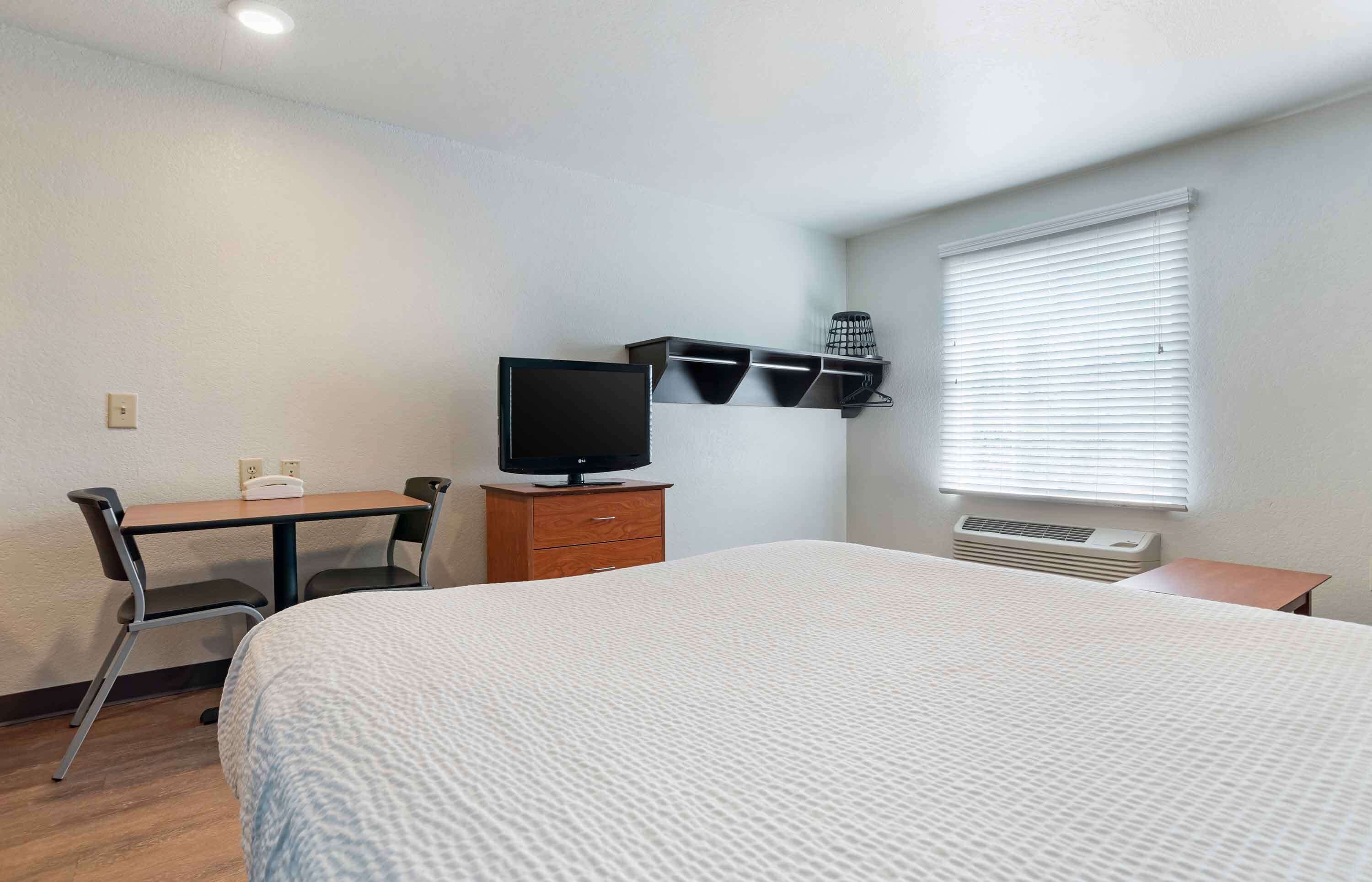 Una habitación de hotel con cama, escritorio, silla, televisor, calefacción y ventana con persianas.