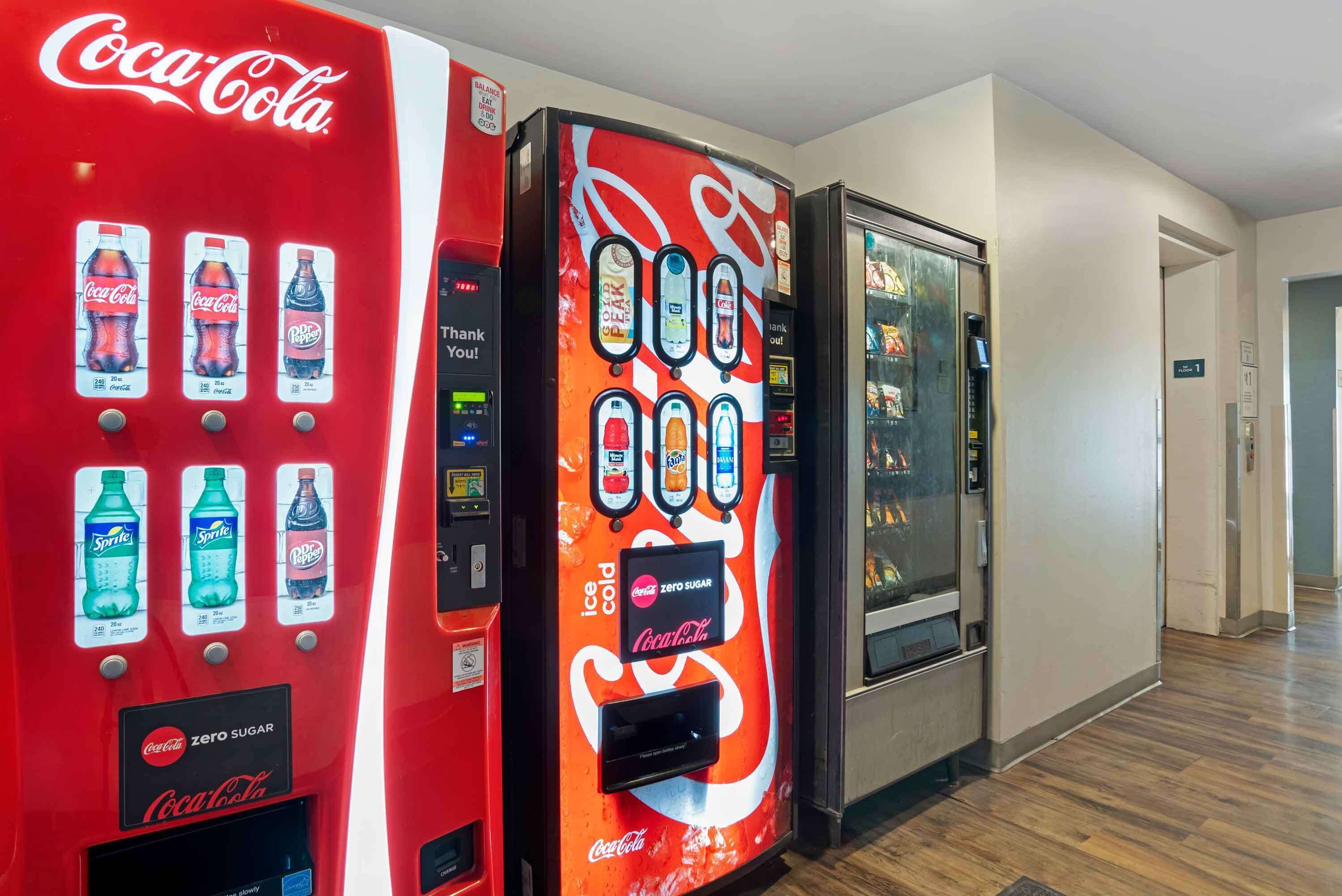 Dos máquinas expendedoras de Coca-Cola en un pasillo, con otra máquina a la derecha.