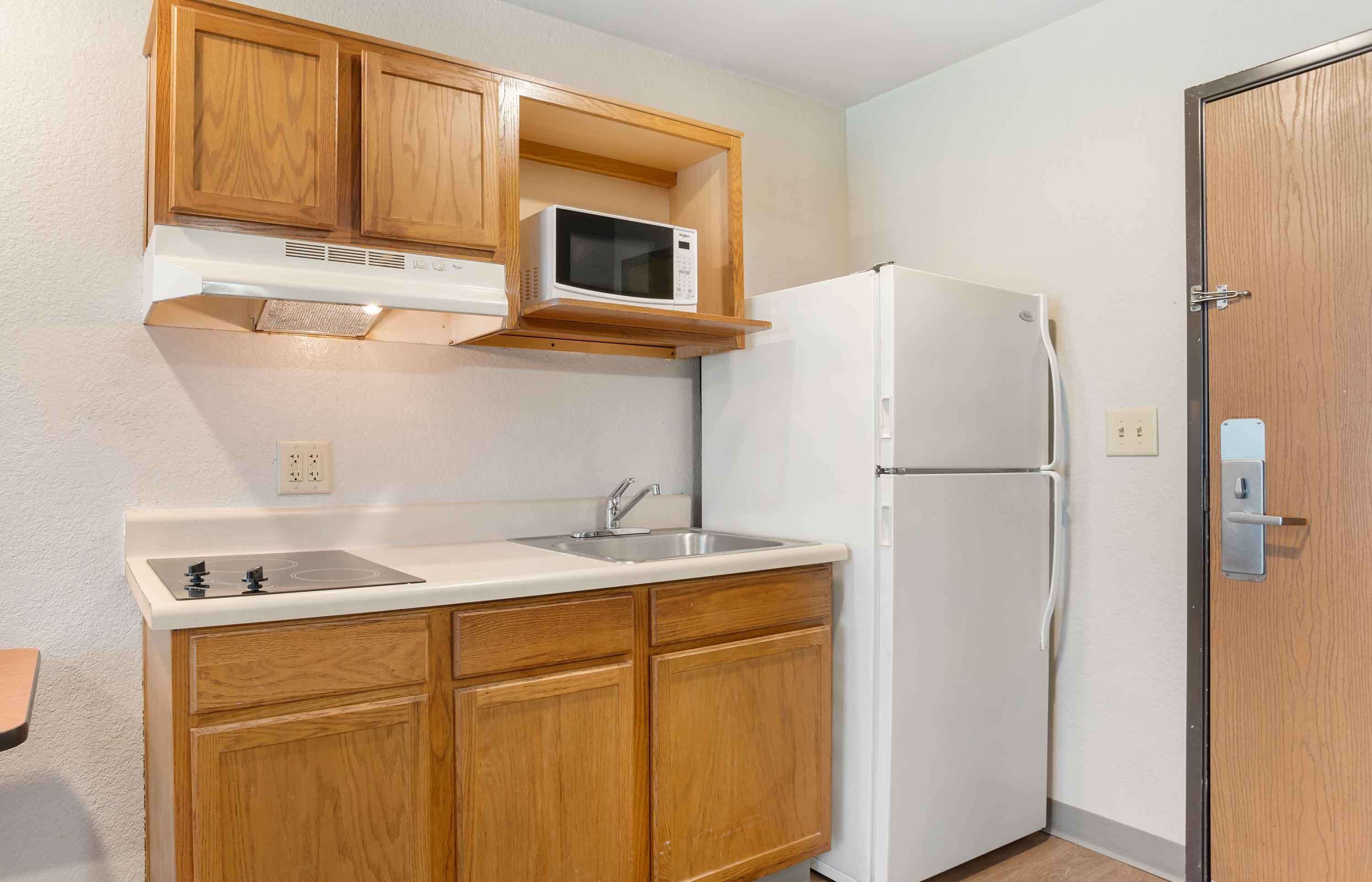 A compact kitchen with wooden cabinets, a microwave, a refrigerator, and a sink.