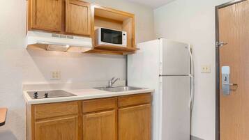 A compact kitchen with wooden cabinets, a microwave, a refrigerator, and a sink.