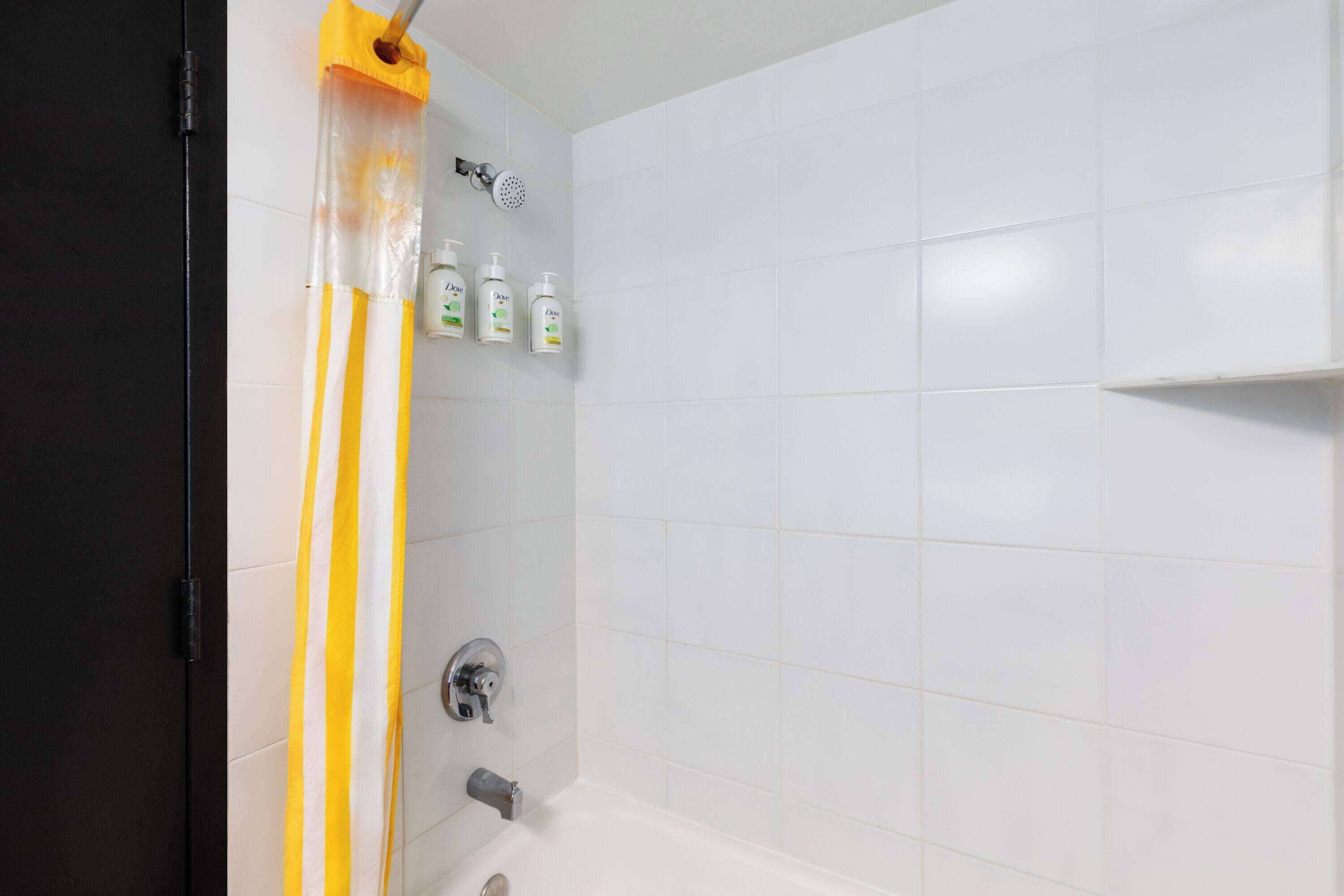 Un baño con azulejos blancos, una cortina de ducha y tres botellas de champú en la pared.