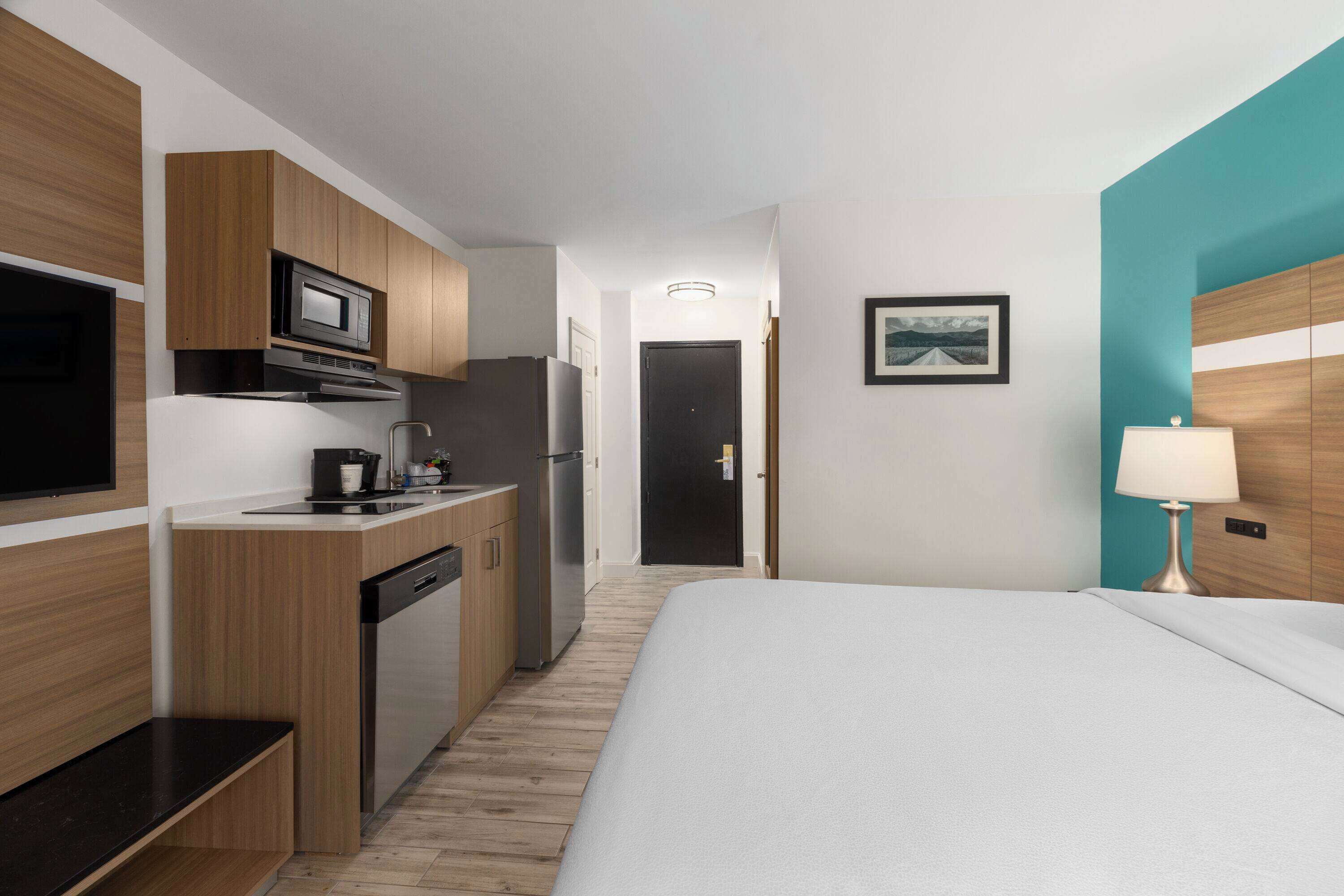 Een kleine hotelkamer met kitchenette, een bed, nachtkastje en lamp.
