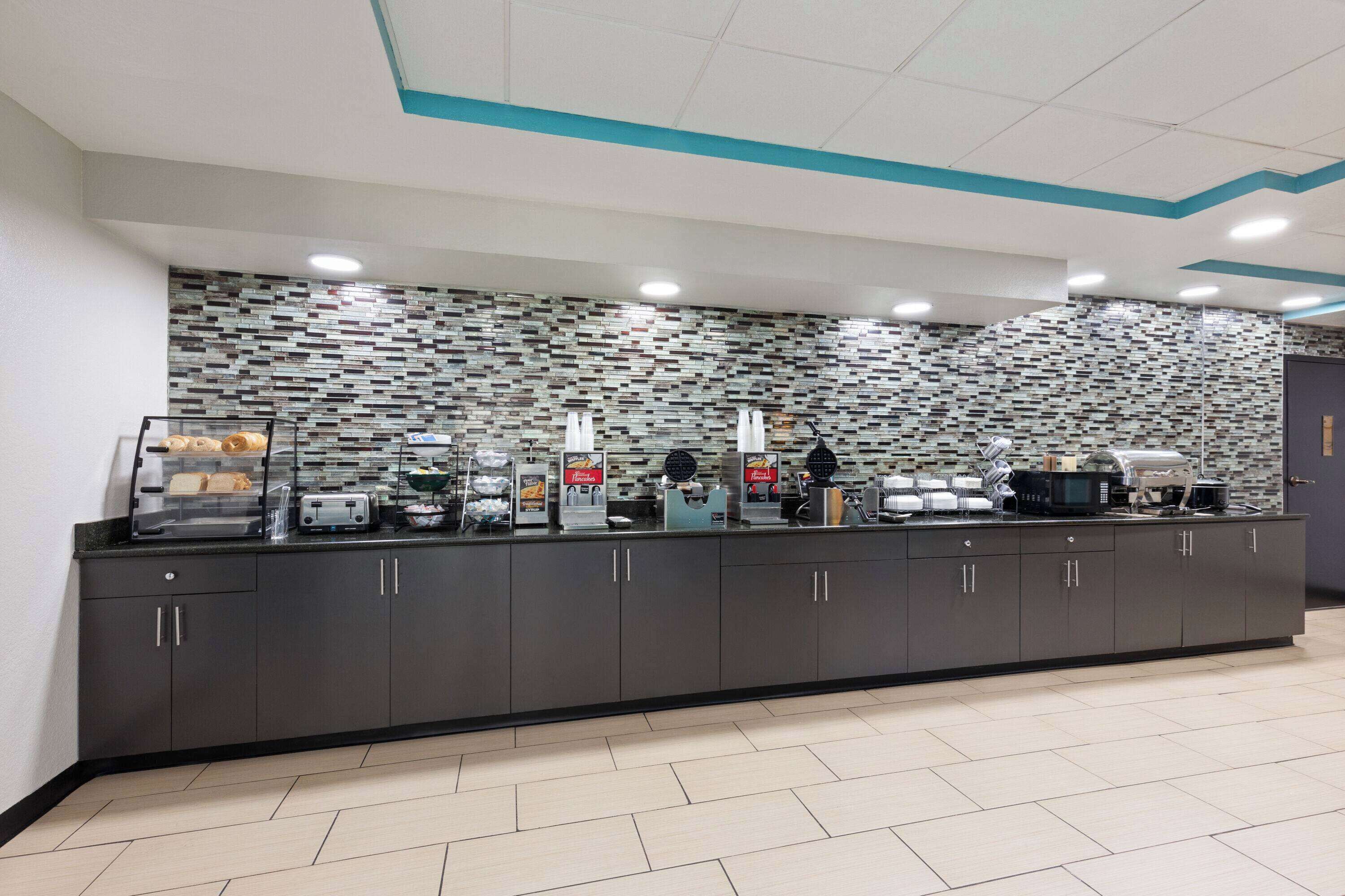 A modern breakfast bar with a patterned backsplash, a microwave, and various food items.