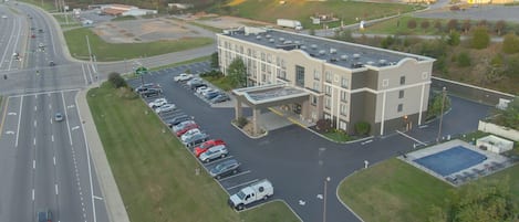 An aerial view of a hotel with a parking lot, a covered walkway, and a swimming pool.