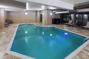 An indoor swimming pool with tiled flooring, a metal pool ladder, and several lounge chairs.