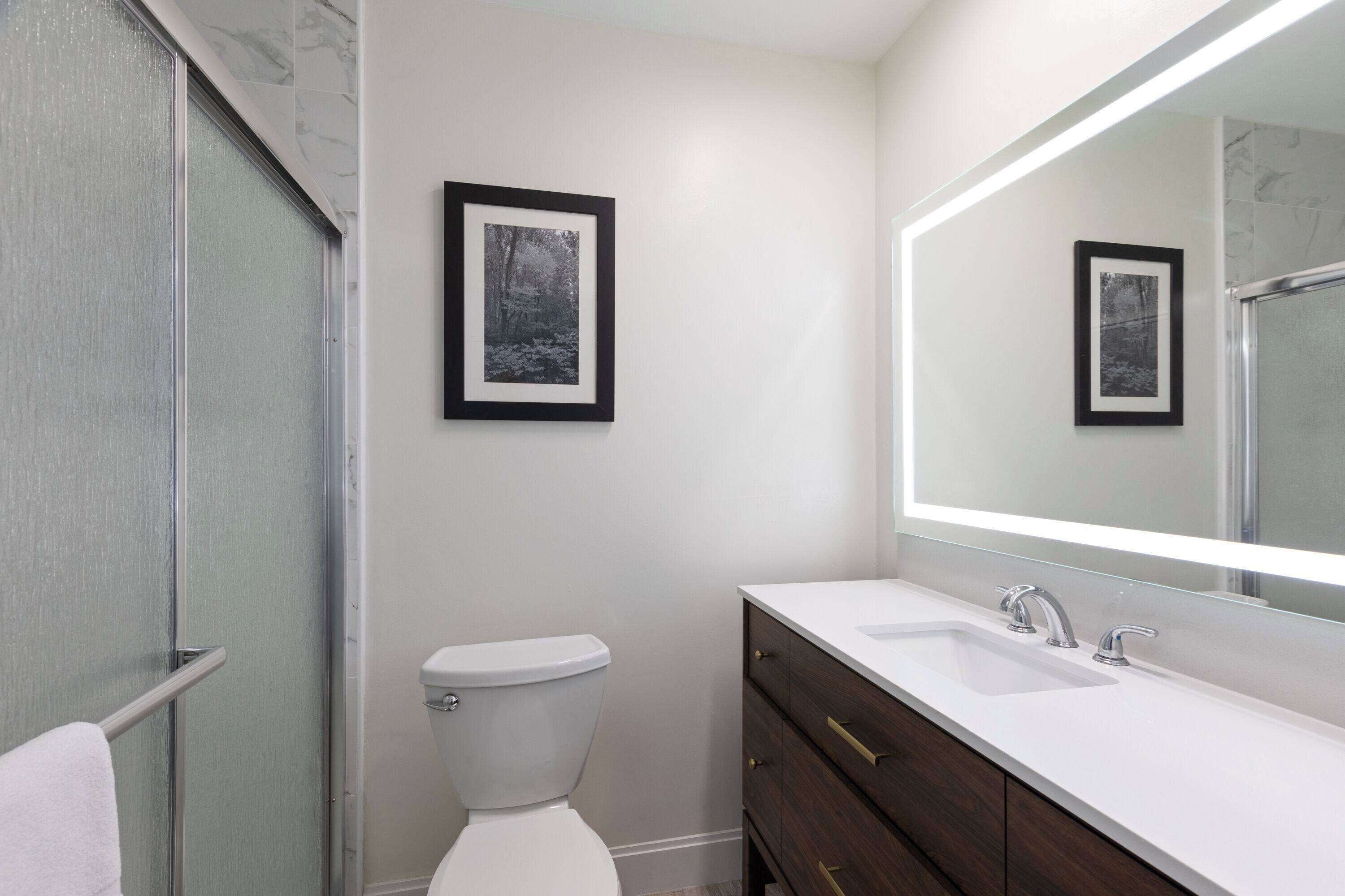 Un baño moderno con inodoro, lavamanos y un espejo grande.