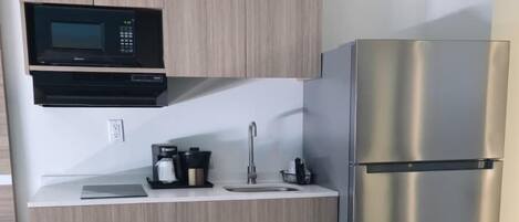 A compact kitchen with a microwave, coffee maker, sink, and stainless steel refrigerator.