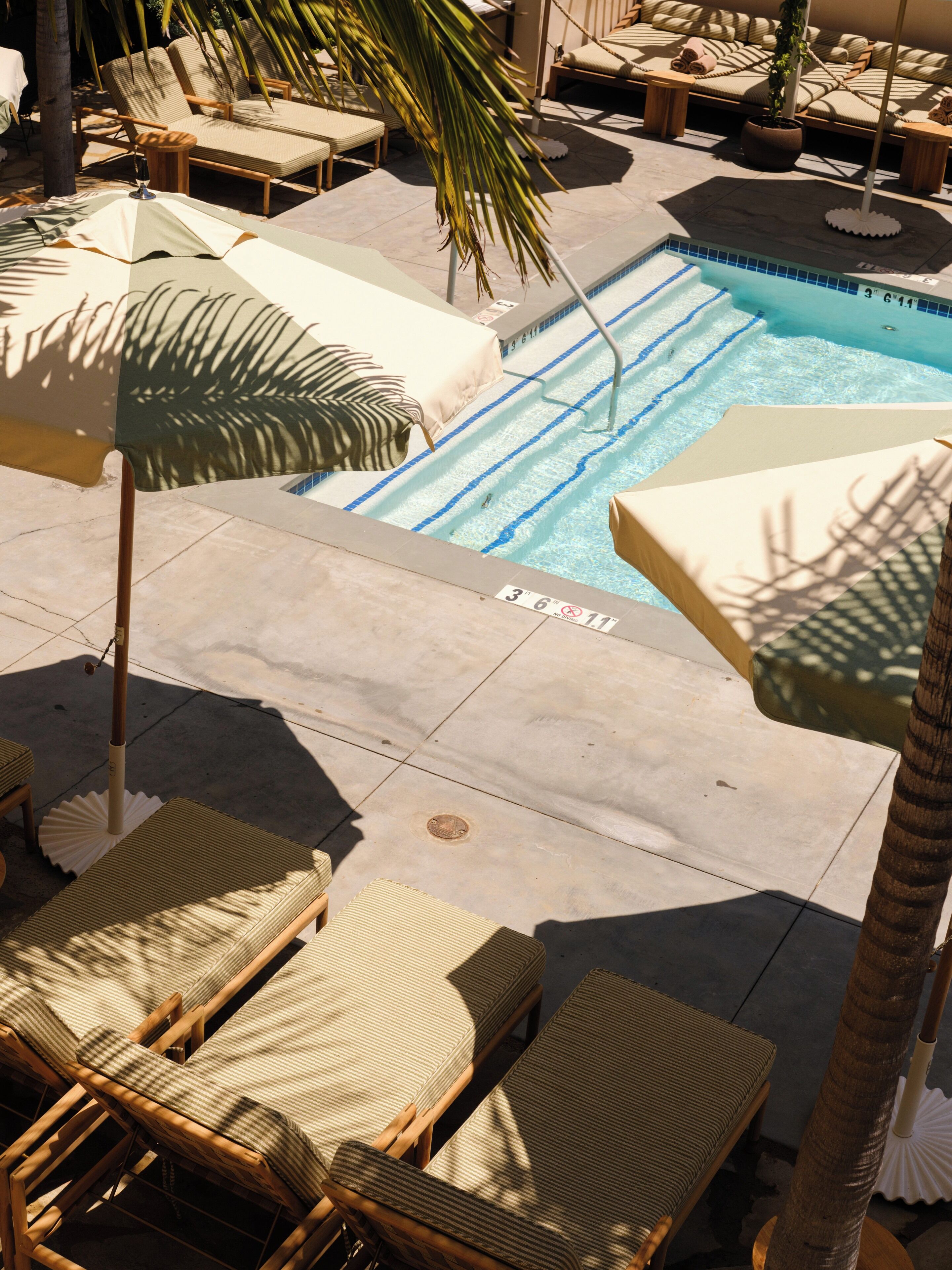 A poolside area with lounge chairs, umbrellas, and a clear blue pool.