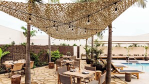 An outdoor patio with tables and chairs, a pool, and a covered area with string lights. - Hotel June West L.A., a Member of Design Hotels (Los Angeles)