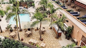 A rooftop pool area with multiple seating arrangements, palm trees, and a stone-tiled patio. - Hotel June West L.A., a Member of Design Hotels (Los Angeles)