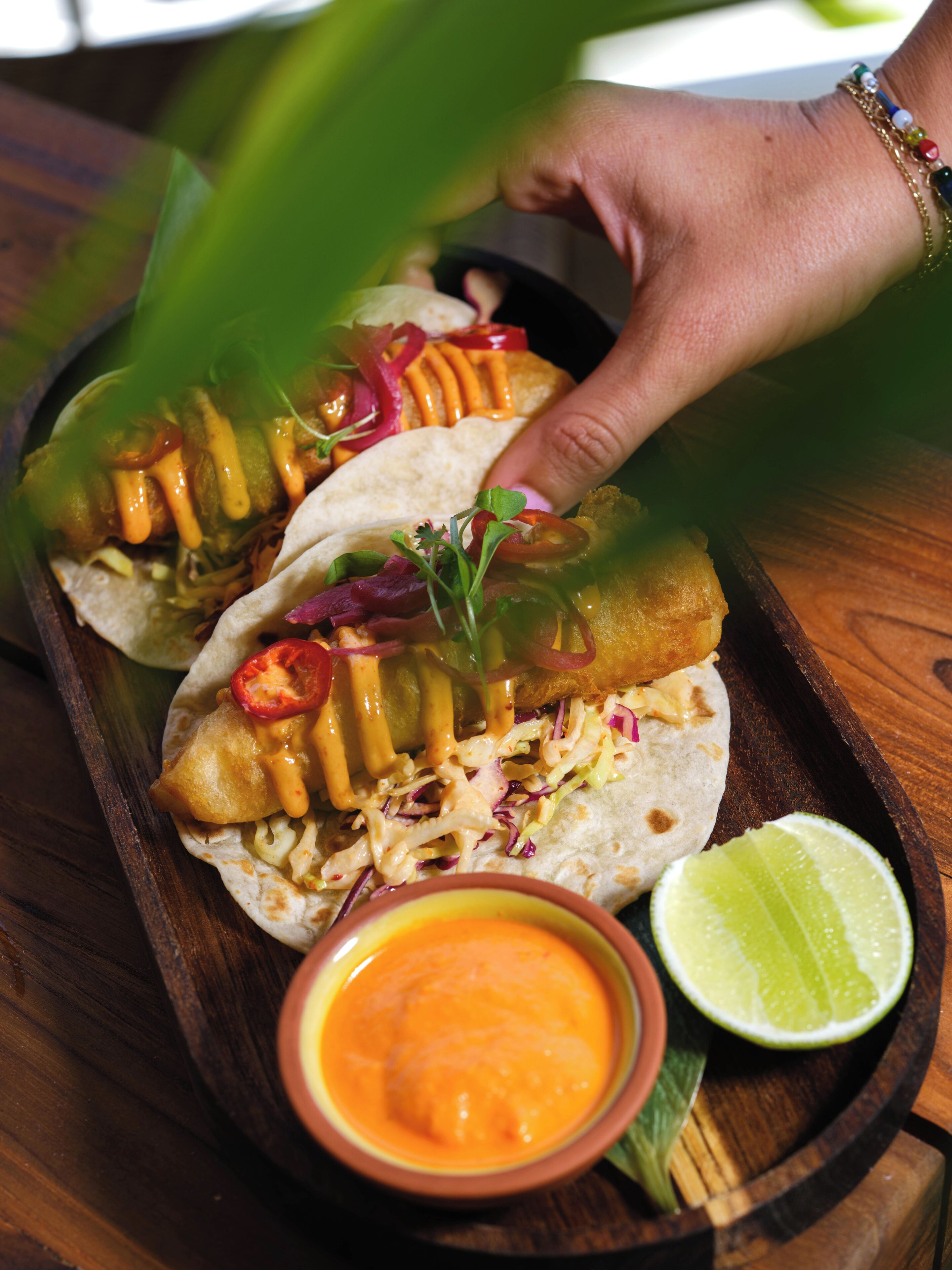 A tray with three tacos, a lime wedge, and a bowl of sauce.