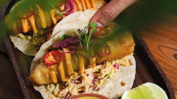A tray with three tacos, a lime wedge, and a bowl of sauce.