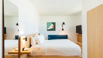 Quarto de hotel moderno com uma cama grande, mesas de cabeceira, televisão e espelho.