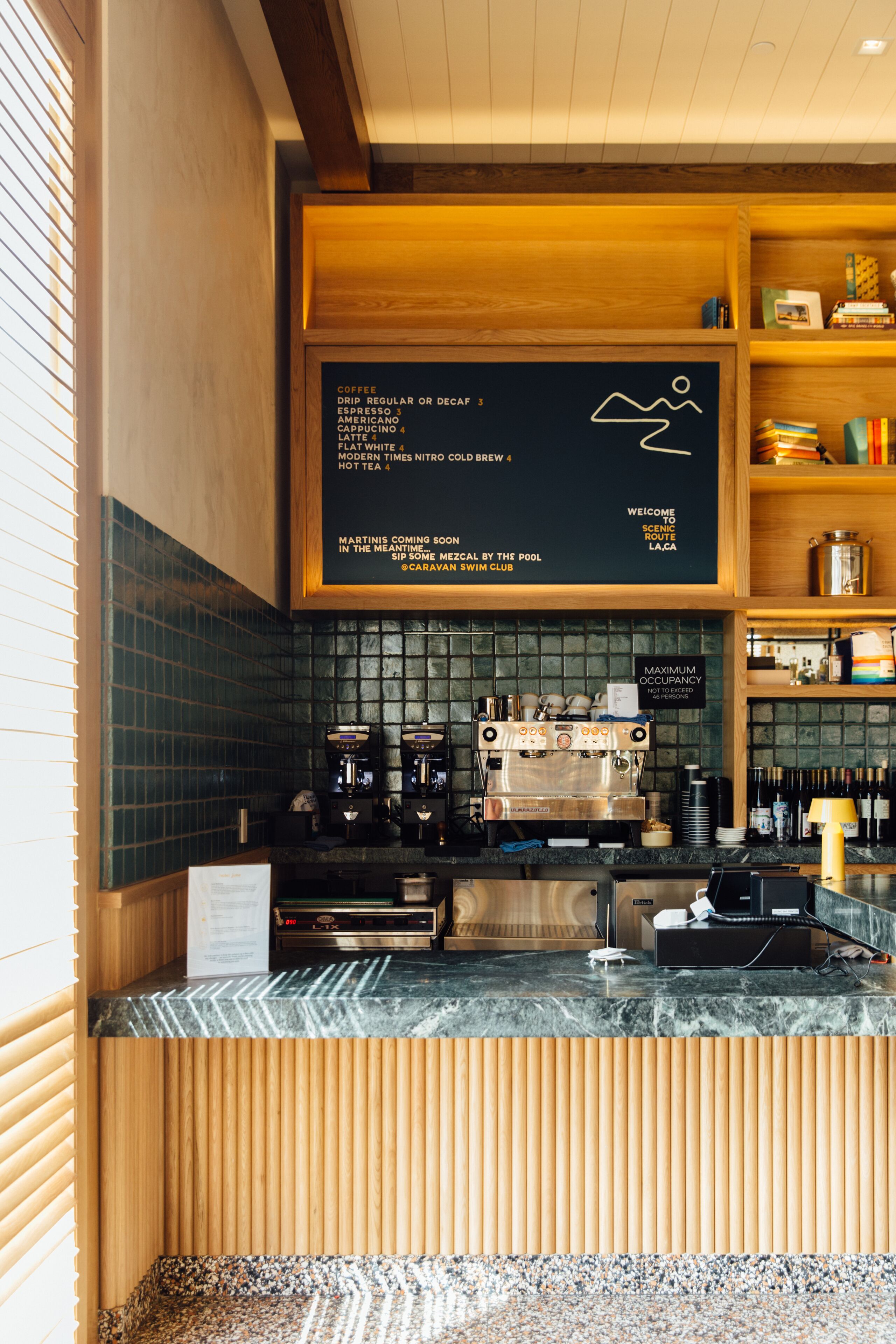 Et caféinteriør med menutavle, espressomaskiner og en trædisk.