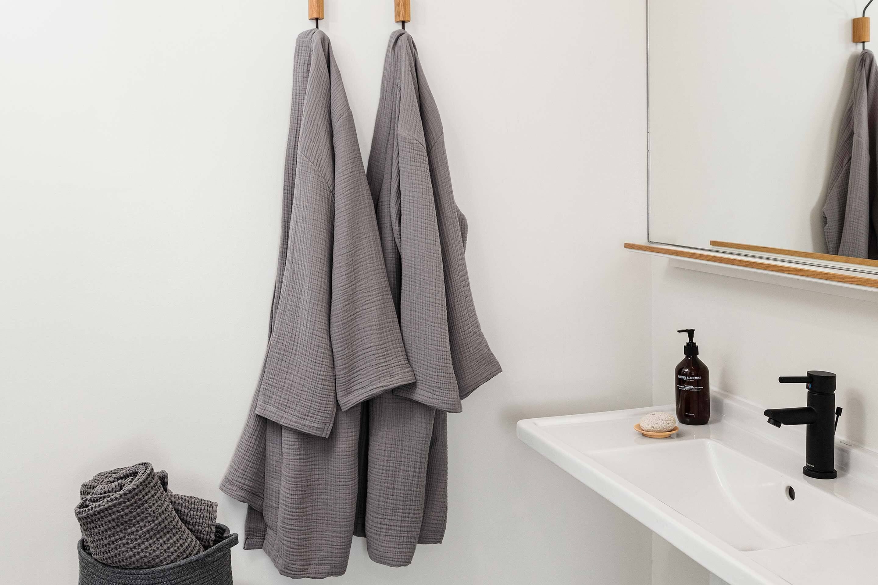 A bathroom with a white sink, a black faucet, a mirror, and two towels hanging on wooden hooks.