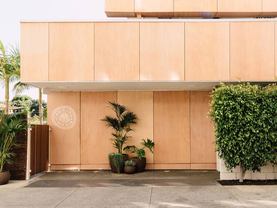 A modern building with a wooden facade, potted plants, and a logo on the wall.