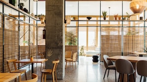 A modern interior with wooden tables and chairs, a concrete pillar, and a view through a bamboo screen to the outside. - Hotel June West L.A., a Member of Design Hotels (Los Angeles)