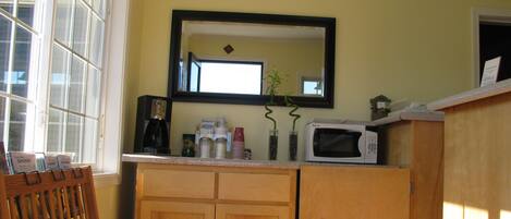 A kitchen with wooden cabinets, a microwave, a coffee maker, and a window with blinds.