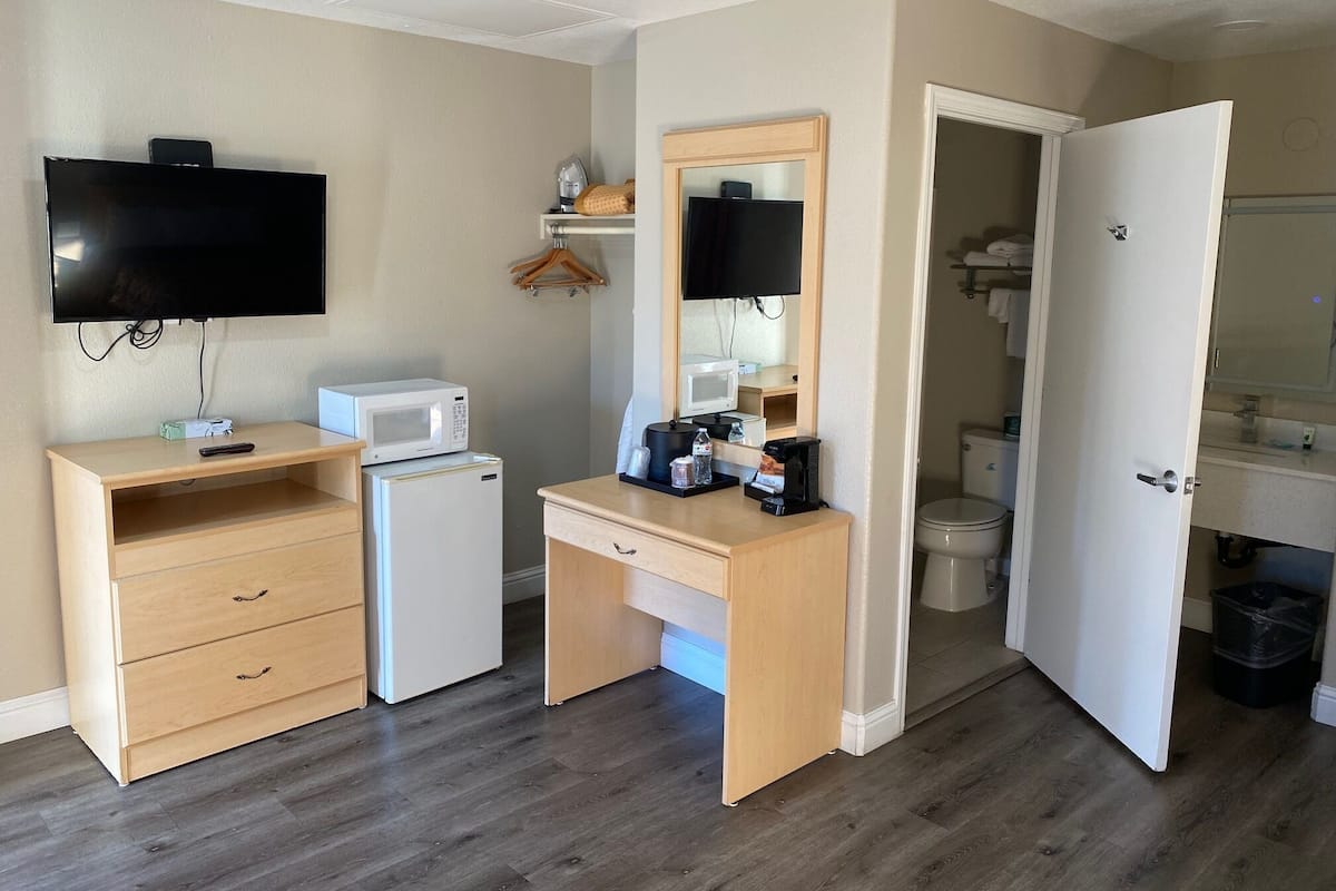 A compact hotel room with a kitchenette, a TV, a small fridge, a microwave, a coffee maker, and a mirror.