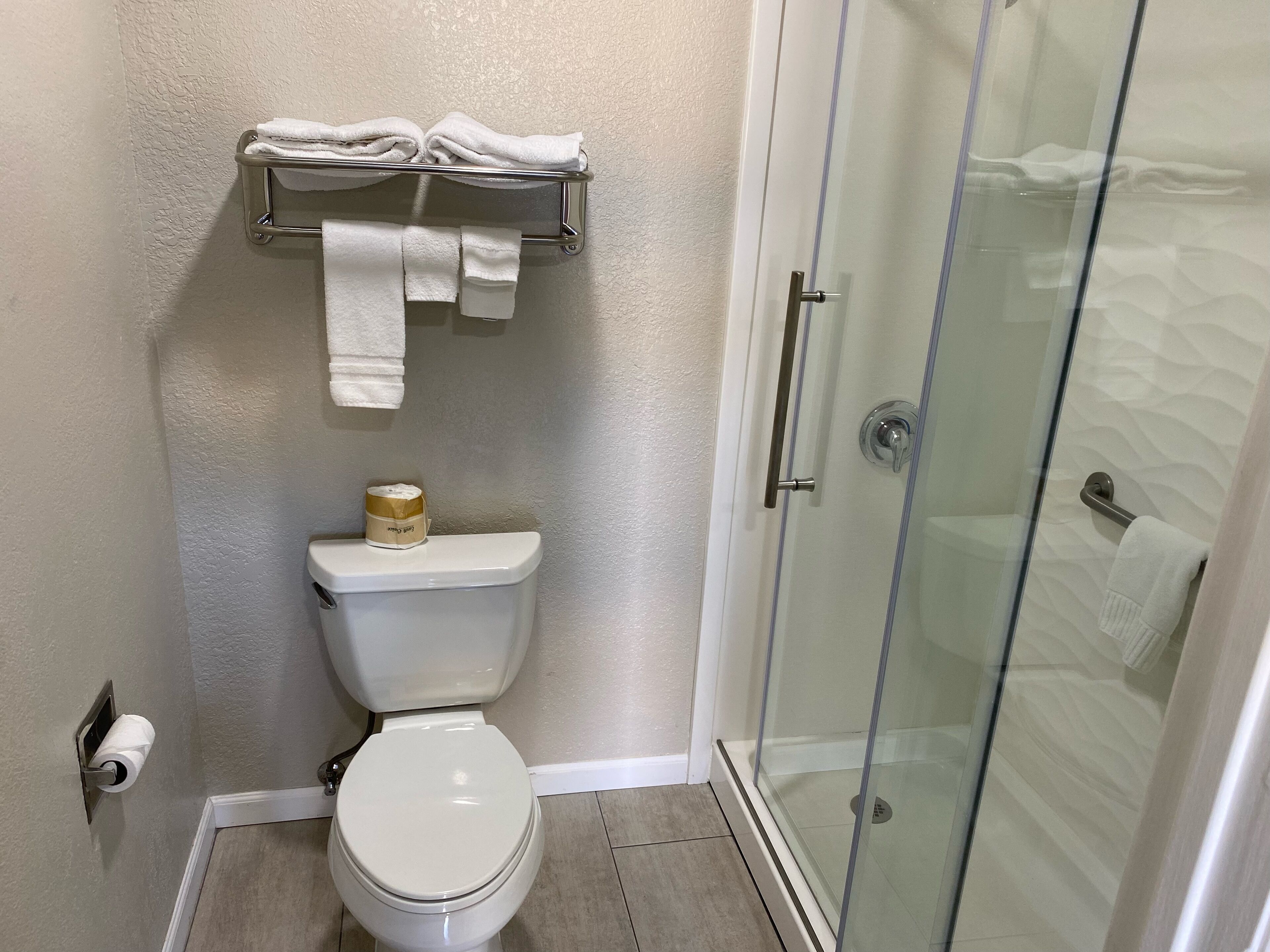 Un baño con inodoro, cabina de ducha de vidrio y toallero con toallas.