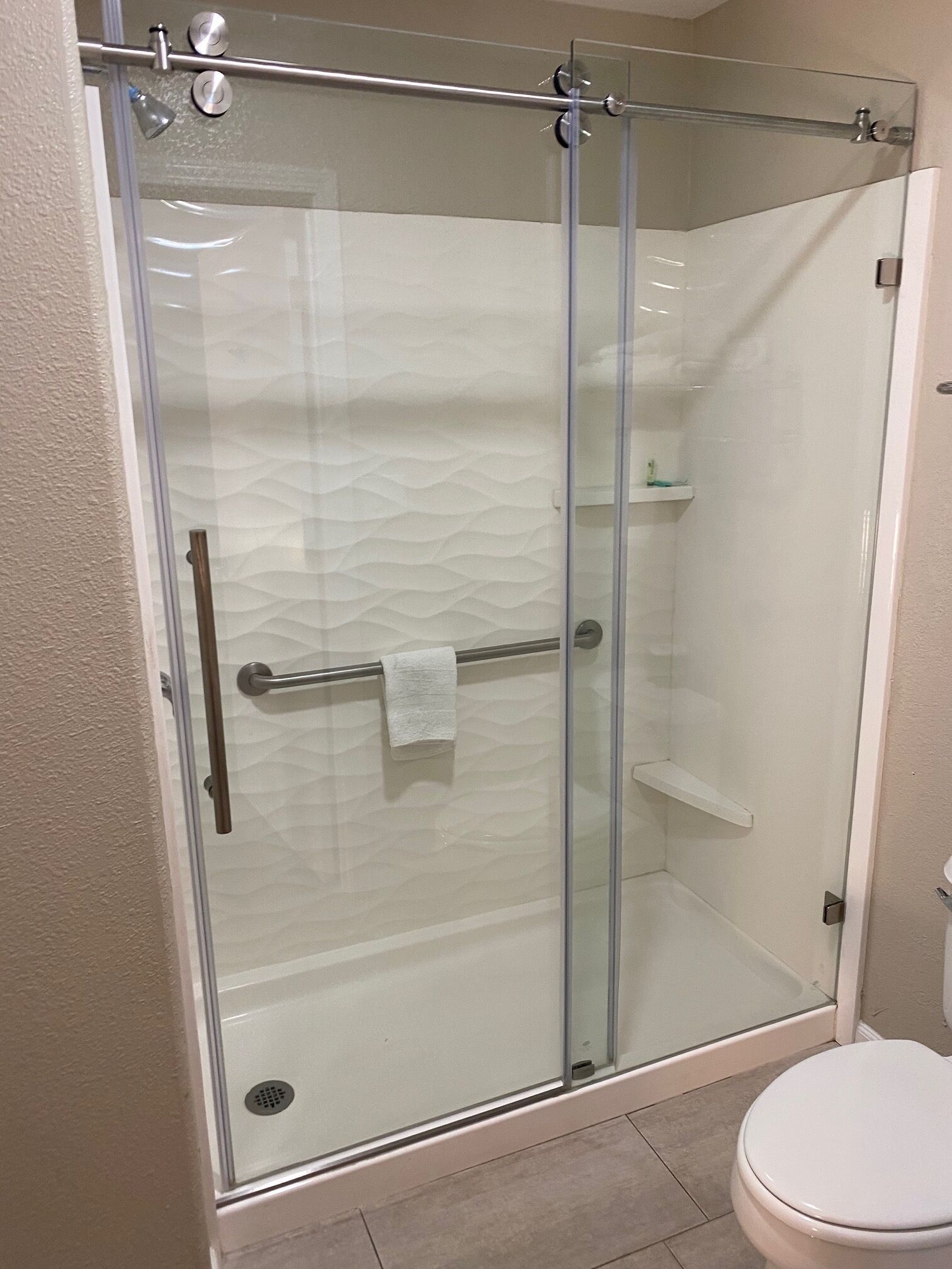 A glass-enclosed shower with a towel rack and a toilet.