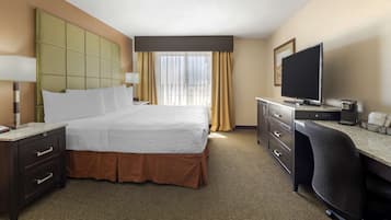 A hotel room with a large bed, a desk, a television, and a window with curtains.