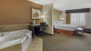 A hotel room with a large bathtub, a desk with a chair, a bed, and a window with curtains. - Best Western Plus Country Inn & Suites (Dodge City)