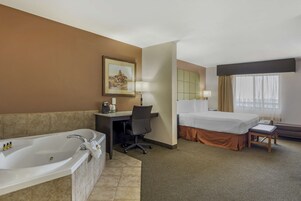 Habitación de hotel con una bañera grande, un escritorio con silla, una cama y una ventana con cortinas.