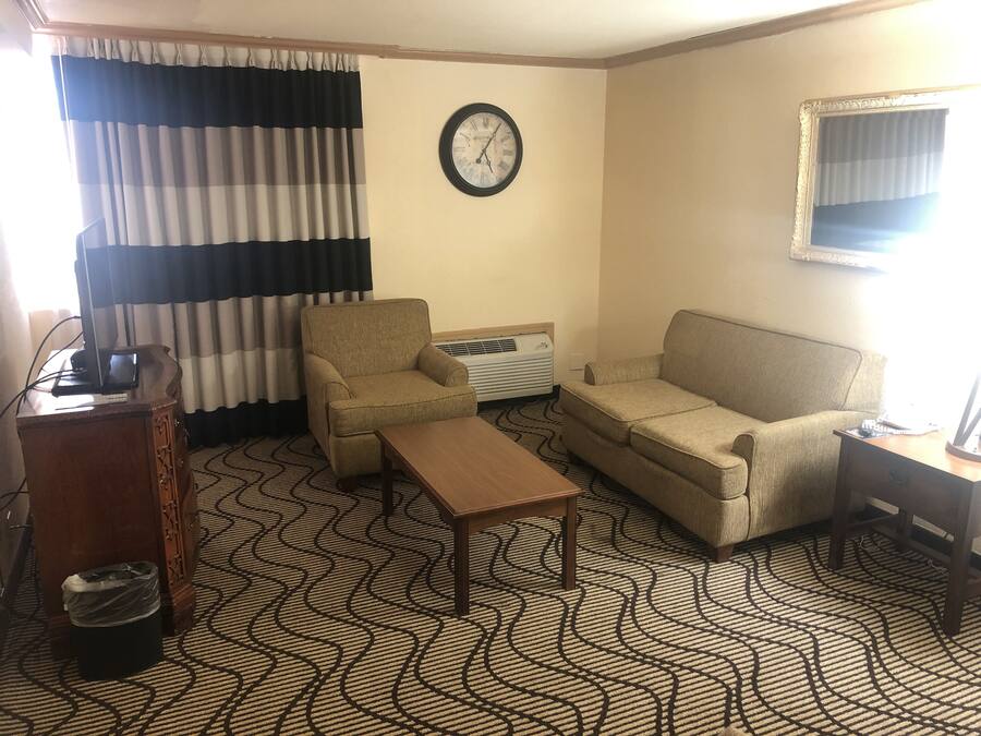 A living room with a sofa, armchair, coffee table, and a clock on the wall.