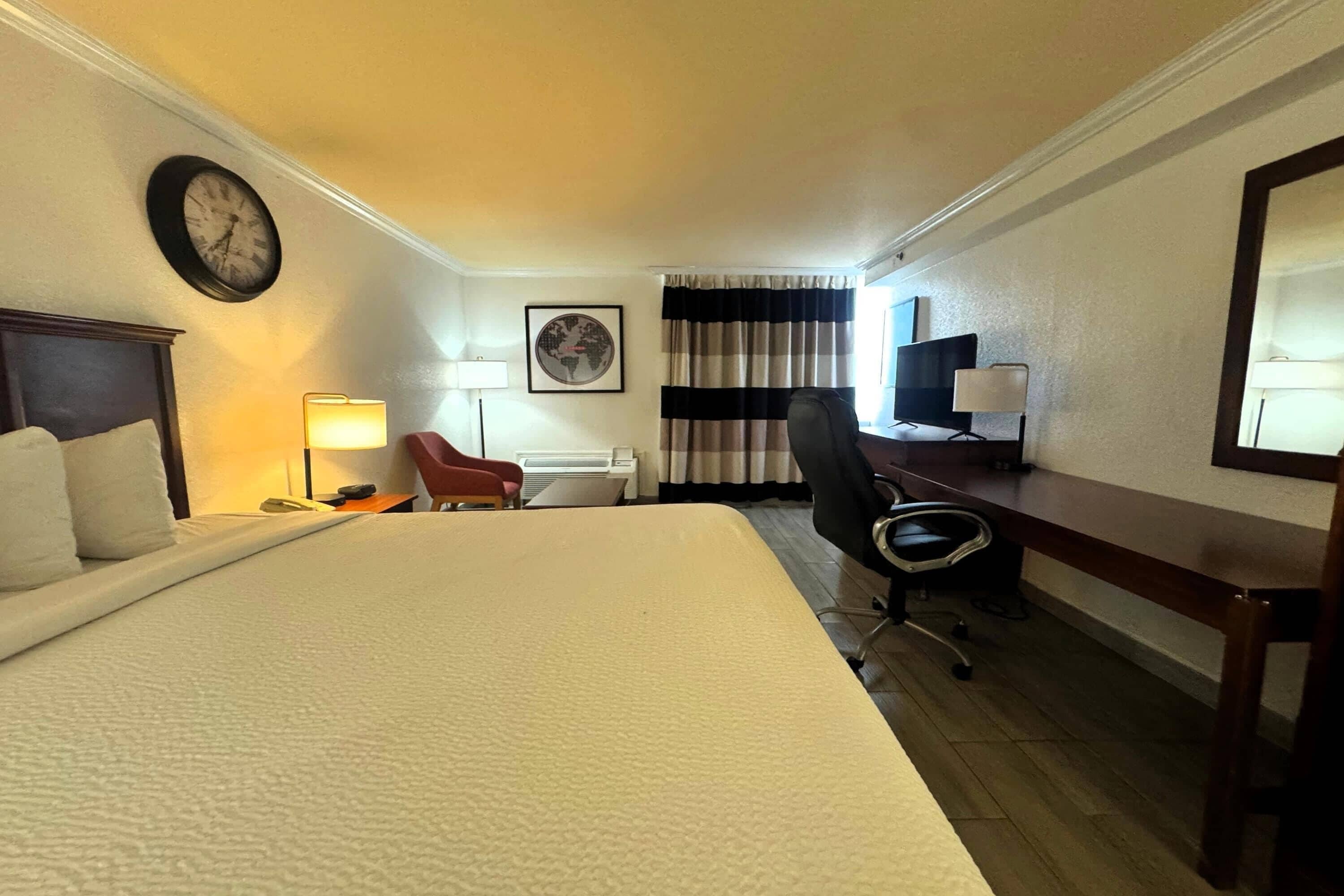 Een hotelkamer met een groot bed, een bureau, een stoel, een lamp, een klok en een wereldbol aan de muur.
