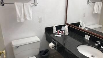 Une salle de bain avec des toilettes blanches, un lavabo noir, un miroir et un porte-serviettes avec des serviettes.