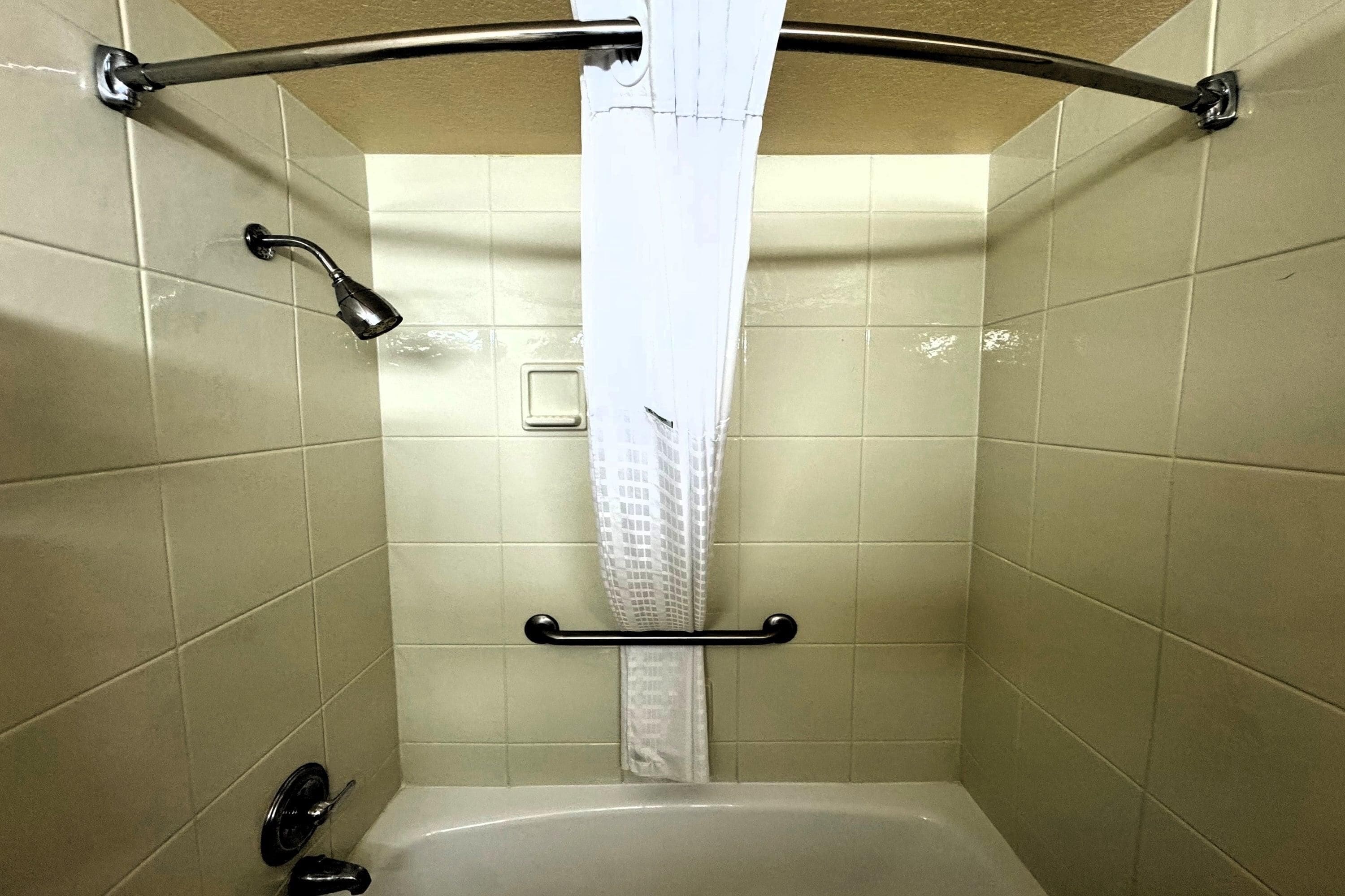 A shower with a grab bar, a handheld showerhead, and a curtain.
