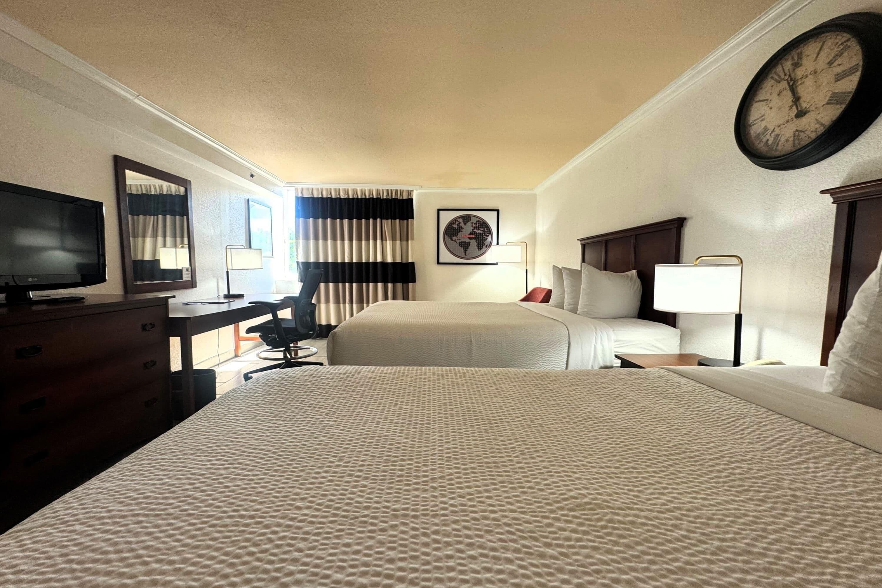 A hotel room with two beds, a desk, a television, a clock, and a window with curtains.