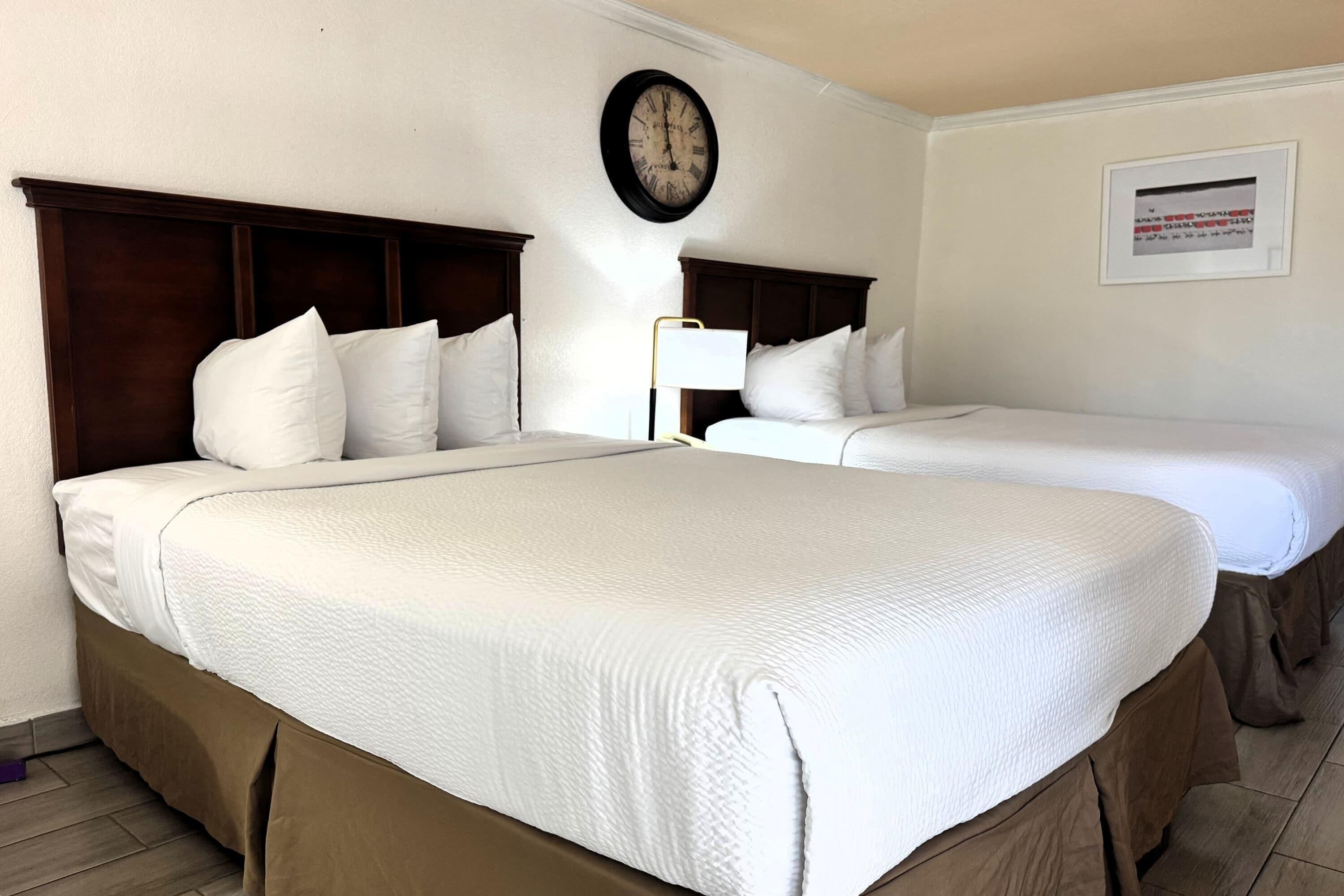 Habitación de hotel con dos camas, un reloj, un aviso enmarcado y una lámpara.