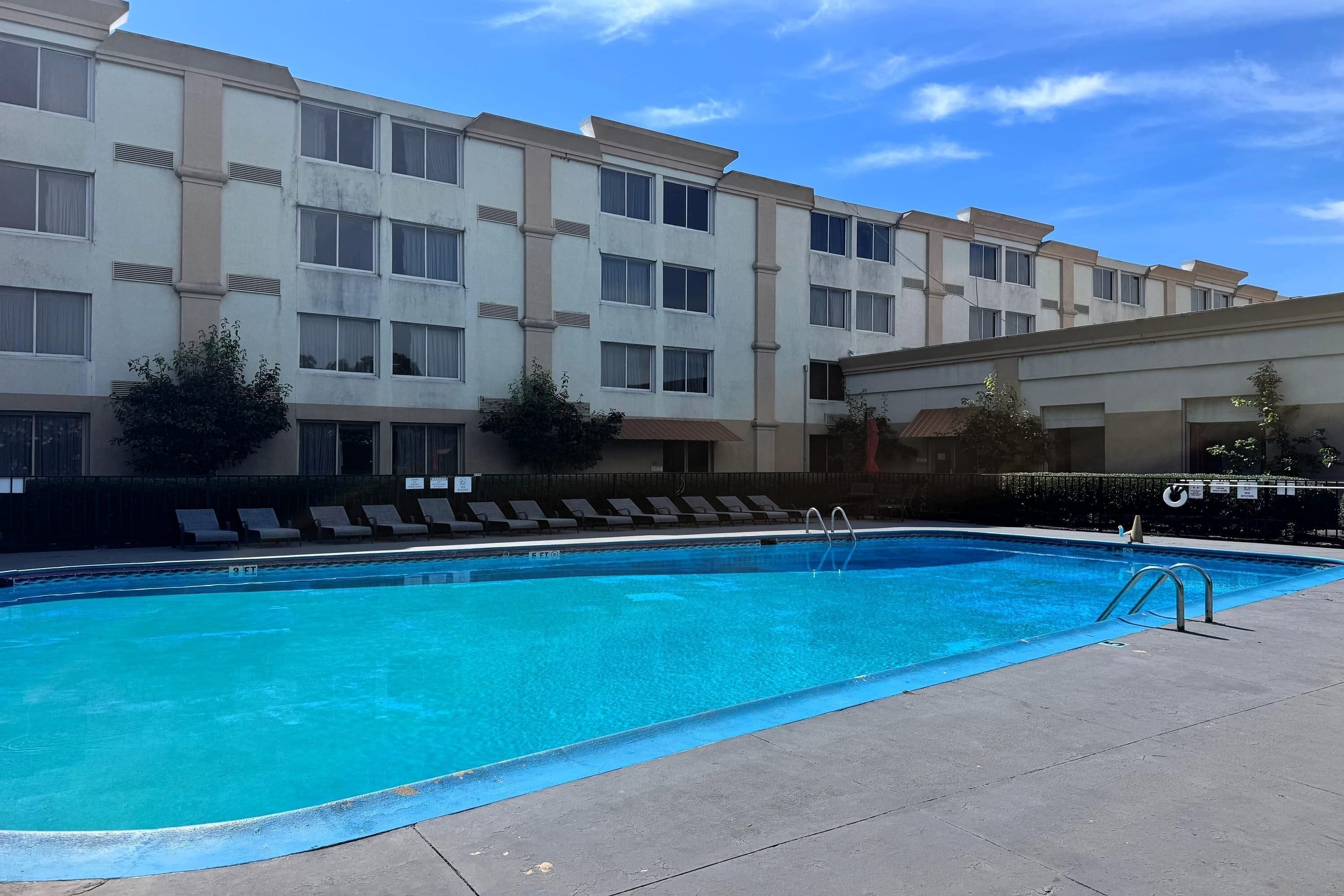 Une piscine avec des chaises longues et un bâtiment doté de nombreuses fenêtres et de balcons.