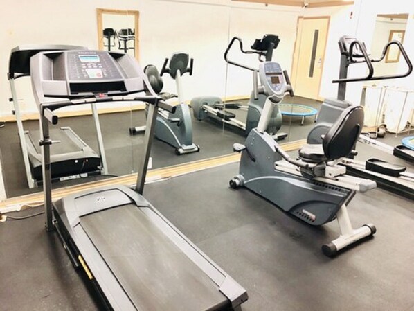 Un gimnasio con diversos equipos de ejercicio, incluyendo cintas de correr, elípticas y bicicletas estáticas.