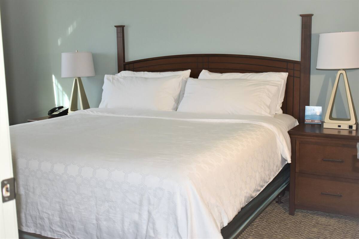 A neatly made bed with a white bedspread and two pillows, flanked by two bedside tables with lamps and a telephone.