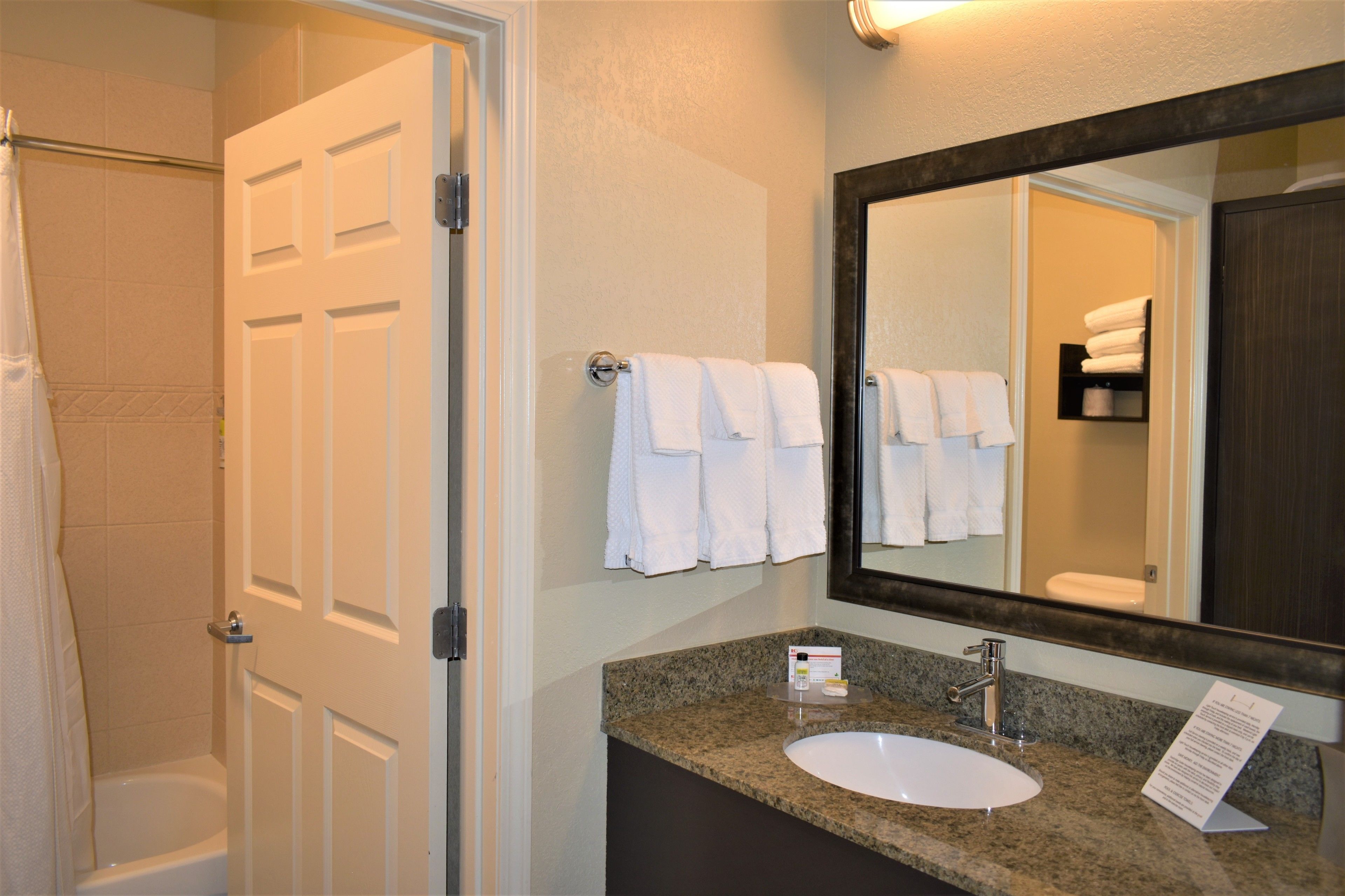 A bathroom with a white bathtub, a sink with a granite countertop, and a large mirror above the sink.