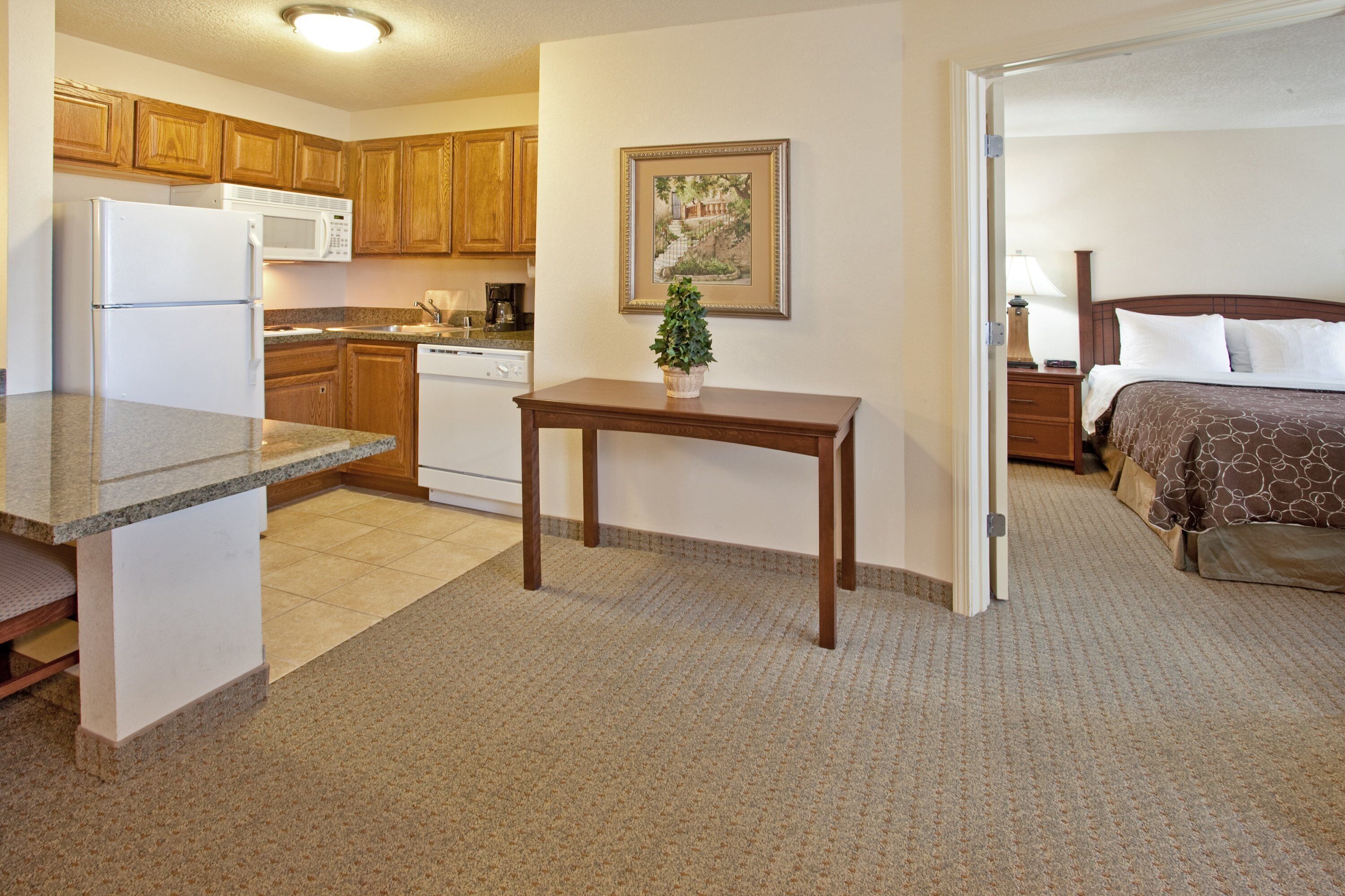 A compact hotel room with a kitchenette, a small dining table, a bed, and a nightstand.