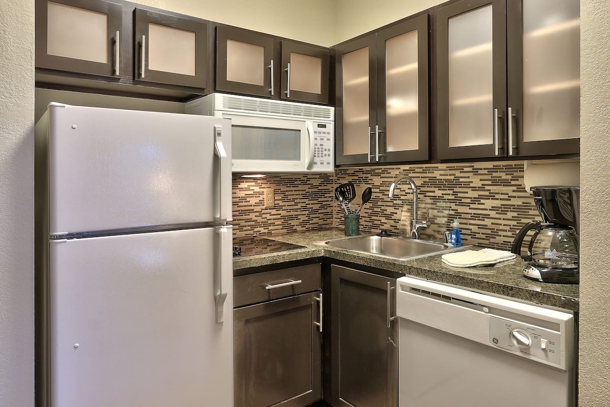 A kitchen with stainless steel appliances, dark wooden cabinets, and a tiled backsplash.
